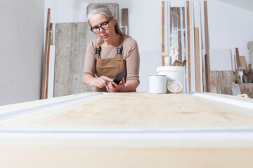 wood crafts, woman artisan carpenter with mobile phone search the internet in her workshop, restoration, diy and handmade works concept
