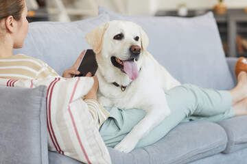 Portrait of young woman lying on couch with dog in cozy home interior, copy space