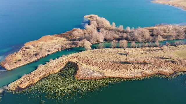 Long peninsula or island and a river in the middle - landform caused by sediment deposition where stream Ljuca flows into lake Plav water in Montenegro. Aerial drone view of promontory on a sunny day.
