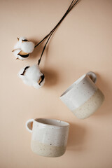 2 ceramic mugs and cotton flowers on a peach background, place for text 