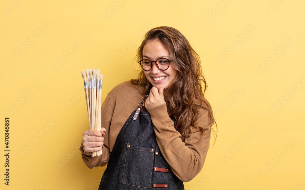 Wall mural hispanic pretty woman smiling with a happy, confident expression with hand on chin. artist with brushes concept