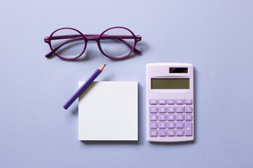 Notepad, colored pencil, calculator, glasses on purple background. workspace. flat lay, top view