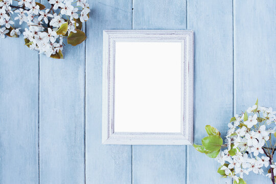 Blank vertical empty picture frame over blue rustic background with spring flowers.