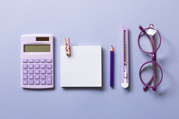 Notepad, colored pencil, cutter, calculator, glasses on purple background. workspace. flat lay, top...