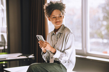 Curly-haired woman sitting on the table with a phone in hands