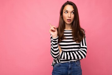 Photo of young european positive thinking and dreaming beautiful brunette woman with sincere emotions wearing casual striped pullover and having an idea isolated on pink background with copy space for