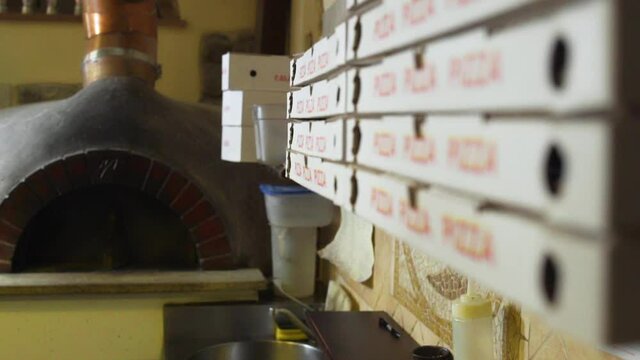 Rack focusing from stacked Pizza boxes to an oven inside an italian Pizzeria