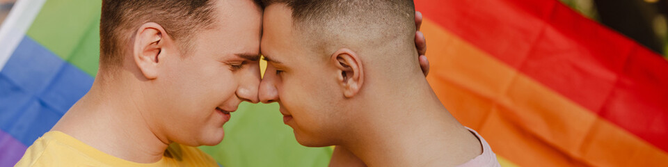 Gay couple hugging while standing with rainbow flag during pride