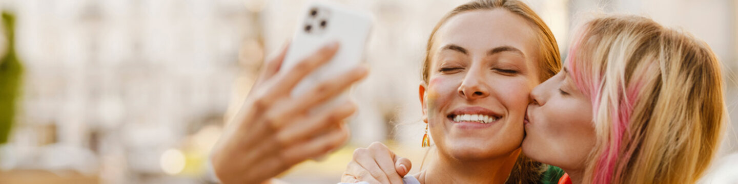 Young Lesbian Couple Taking Selfie On Cellphone During Pride Parade