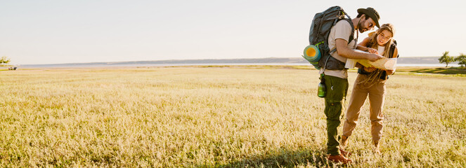 White couple with backpacks examining map while hiking together