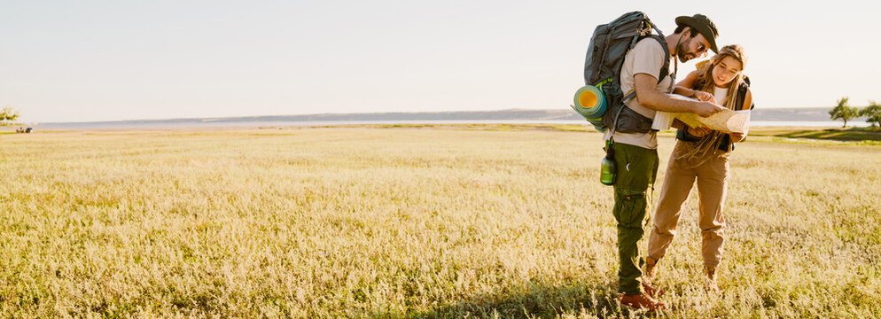 White couple with backpacks examining map while hiking together