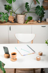 blank opened notebook with cup of coffee and memo note on table. work space with mug of coffee, plat in pot Stylish interior of home office room