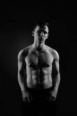 Fototapeta na wymiar Black and white portrait of an athletic guy on a black background.