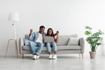 African american couple using laptop, celebrating win