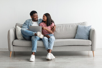 African American couple sitting on couch, using laptop