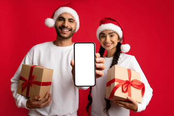 Cheerful Arab Couple Holding Christmas Presents And Showing Blank Smartphone