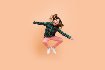 Photo of funny pretty schoolgirl wear plaid outfit jumping high arms sides smiling isolated beige...