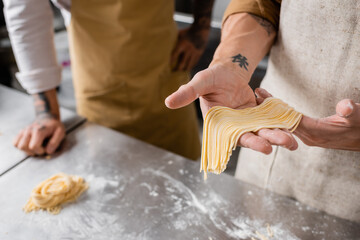 Cropped view of chef holding raw spaghetti near colleague in kitchen