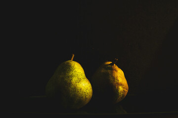 Fototapeta na wymiar Two pears are placed in dark field. Those pears are shining dull in the dark.