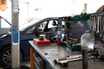 Photo of a metal table with working tools for working and repairing an auto against the background of a blue passenger car at a service station being repaired with an open hood