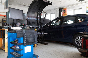 Obraz na płótnie Canvas Photo of a machine for balancing wheels and repairing tires of an auto against the background of a blue passenger car at a service station at a repair with an open hood