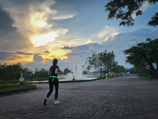 Asian woman jogging in city park at sunset short in low light.