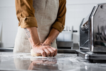 Cropped view of chef making dough near pasta maker machine on table in kitchen