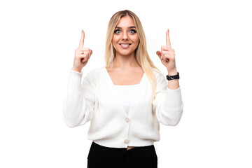 Photo of a beautiful positive happy smiling young blonde woman with makeup in a stylish white knitted sweater and black pants shows fingers up isolated on a white background with empty space for text