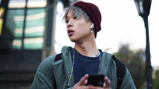 Handsome Asian man texting by phone and looking to the sides outdoors