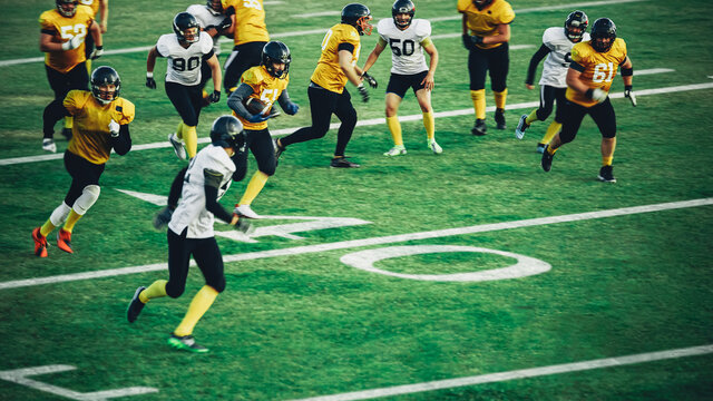 American Football Field Two Teams Compete: Successful Player Jumping Over Defense Running to Score Touchdown Points. Professional Athletes Compete for the Ball, Tackle, Fight for Victory.