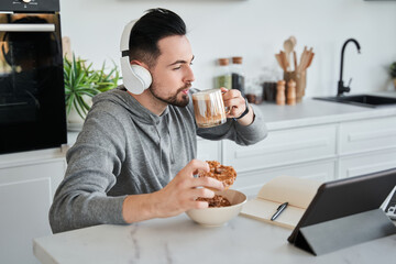 Handsome man wearing headphones looking at the laptop screen with pleasure smile