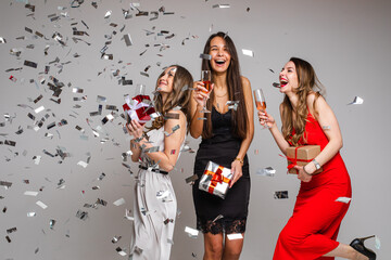 Three girls with drinks having fun under confetti.