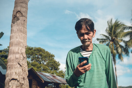 An Old Filipino Farmer Checks His Social Media. Tech Savvy Senior Citizen. Rural Village Scene