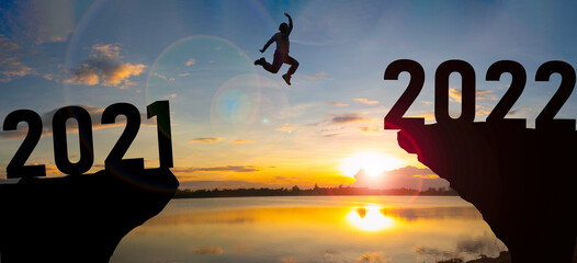 Happy new year Silhouette sunset background. A man jumping over cliff and jump between 2021 and...