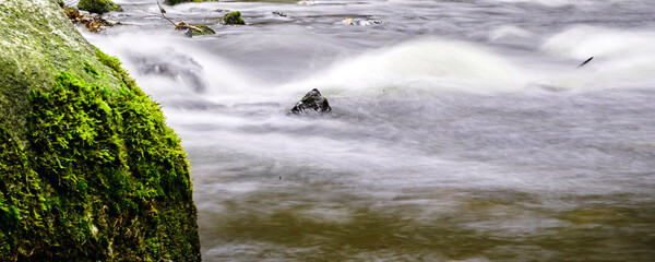 Abstract long exposure of a foaming brook from whose surface a pointed angular stone protrudes