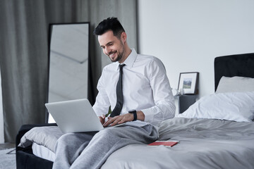 Businessman wearing formal suit sitting at the bedroom at the edge of the bed