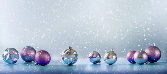 Pink and purple Christmas tree bulbs on blue background with falling snow, banner size
