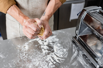 Cropped view of chef holding dough near pasta maker machine and flour on table