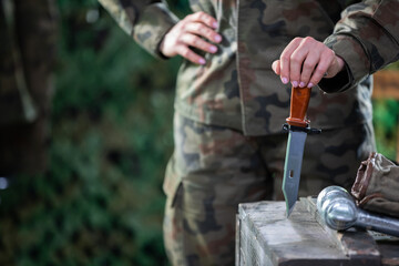 A woman in moro garb stabs a knife into a wooden crate. The soldier's equipment.