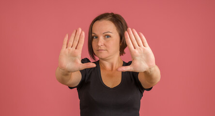 woman in black t-shirt put out her palms in front, stop sign, pink background