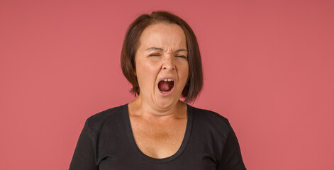 brunette woman in black t-shirt yawns opening her mouth on pink background