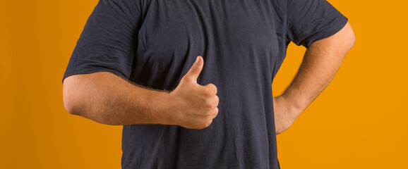 man in black t-shirt shows thumbs up on yellow background