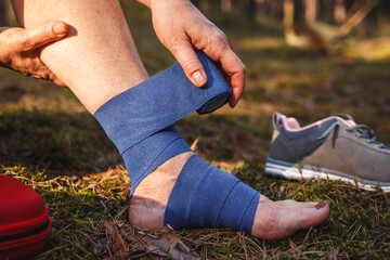 Injured woman using elastic bandage for fixation sprain ankle. Health accident during hiking...