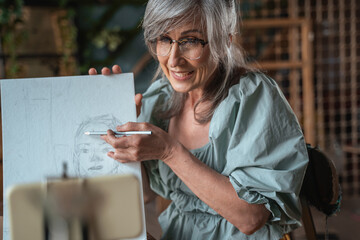 Artist holding pencil and showing something at her drawing while teaching
