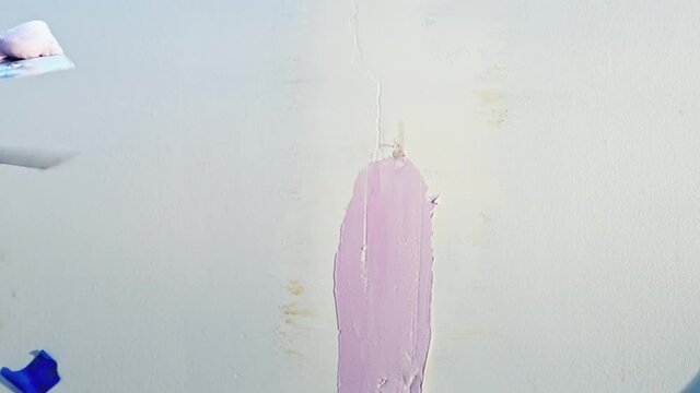 Painters is adding pink patching compound on walls with putty knife close up