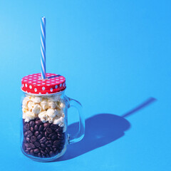 Full jar, with handle, closed. In the jar, coffee beans, popcorn. Red lid, white dots. Straw...