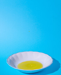 White plate. Oil in a plate. Harsh shadow. Blue background. Text space. Cooking, fresh, organic, raw, oil, concept. Minimal style.