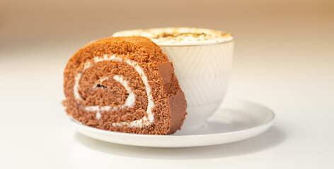 Chocolate sponge roll with a vanilla flavour filling and fresh coffee in the cup, chocolate swiss roll