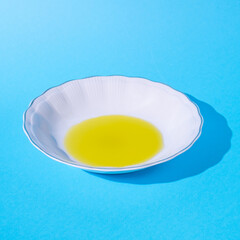 Plate, white. Oil in a plate. Harsh shadow. Blue background. Text space. Cooking, fresh, organic, raw, oil, concept. Minimal style.