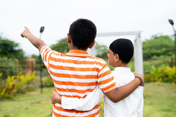 Back view of unrecognizable multiethnic friends walking by placing hands on shoulder at park -...